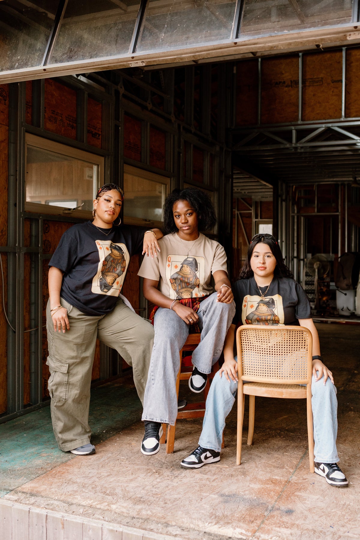 Three people sitting in a rustic indoor setting with chairs and a wooden floor.