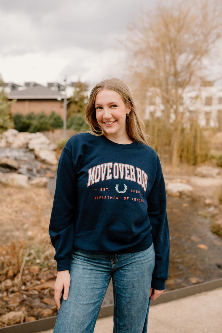 Person wearing a navy sweatshirt with text standing outdoors near a stream.