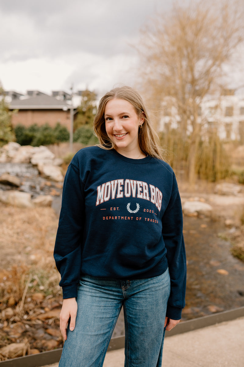 Person wearing a navy sweatshirt with text standing outdoors near a stream.