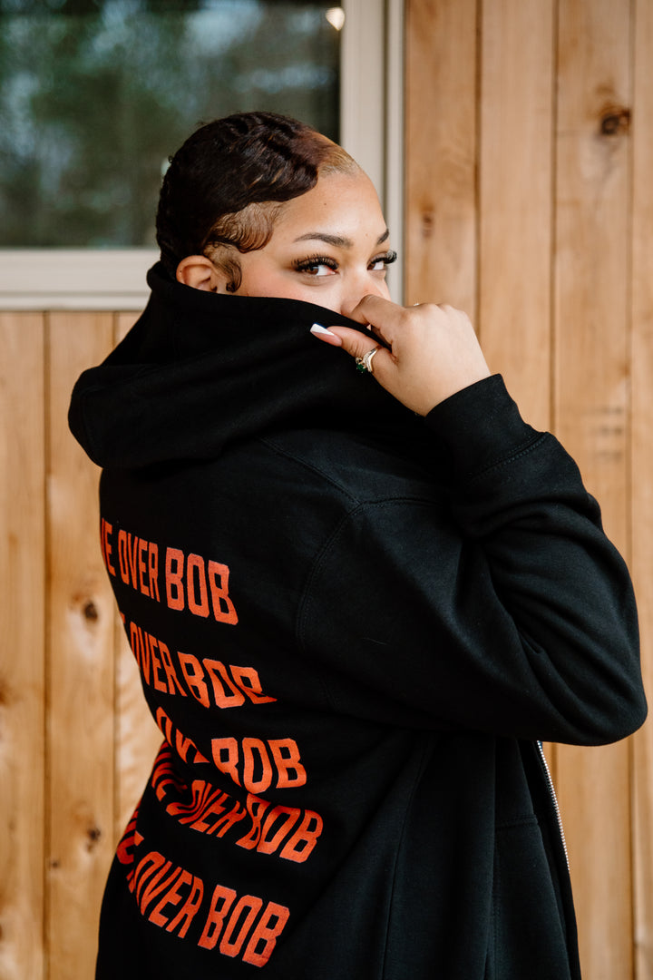 Person wearing a black hoodie with orange text, standing in front of a wooden wall.